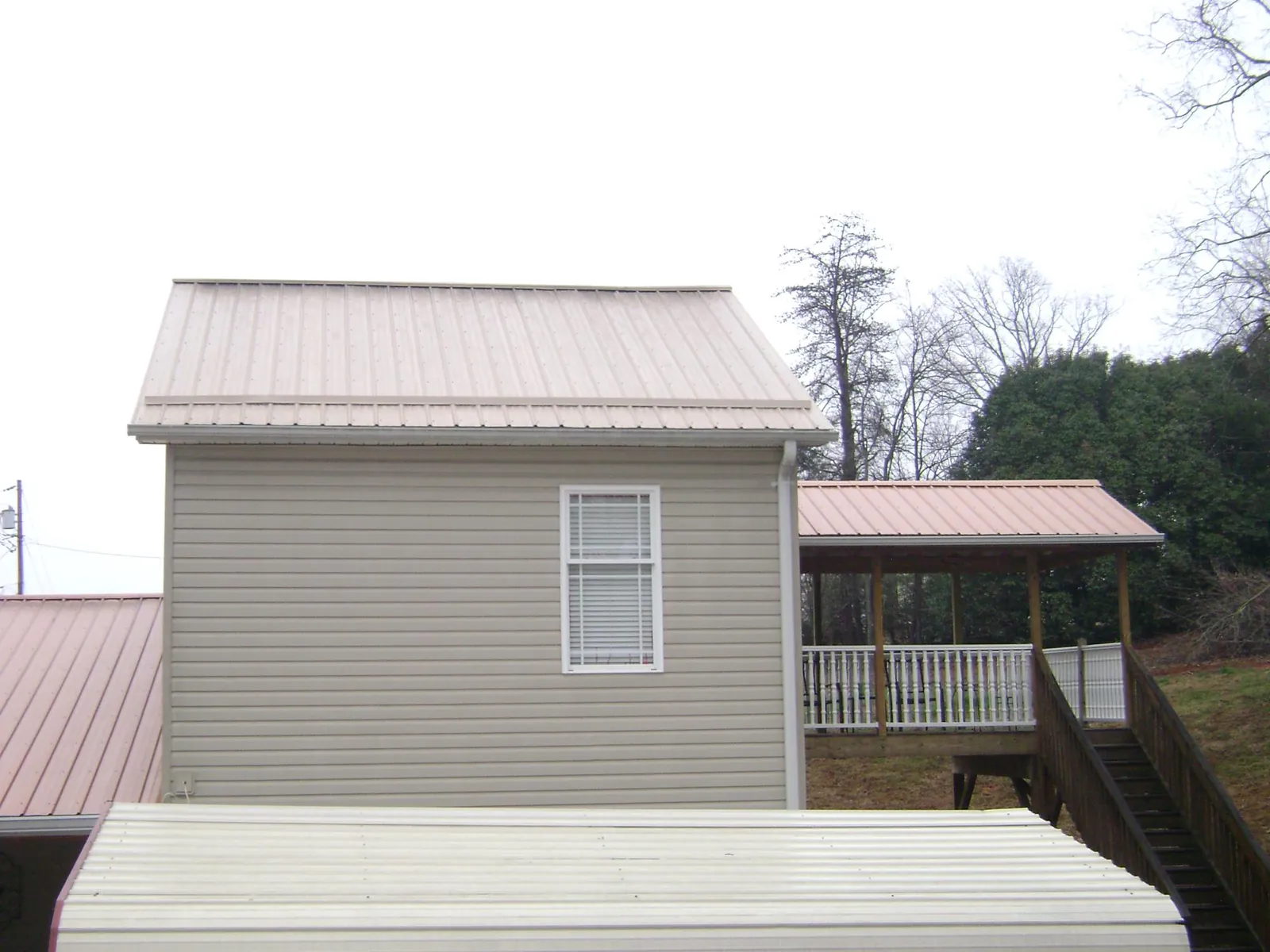 Tan metal roofs on a two story addition and attached porch, from a Roof Replacement job in Stewart